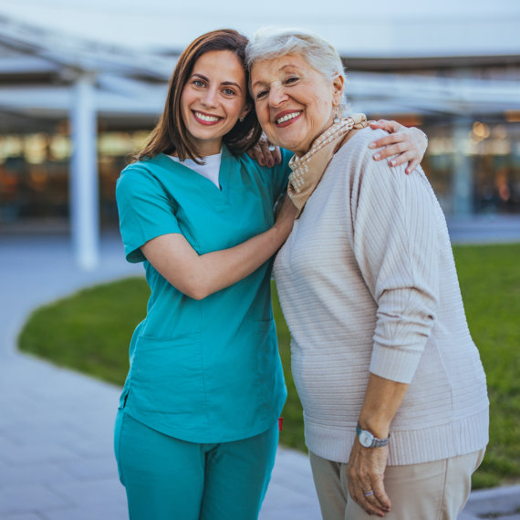 A cheerful nurse embraces an elderly woman