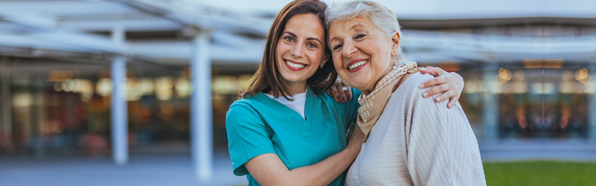 A cheerful nurse embraces an elderly woman